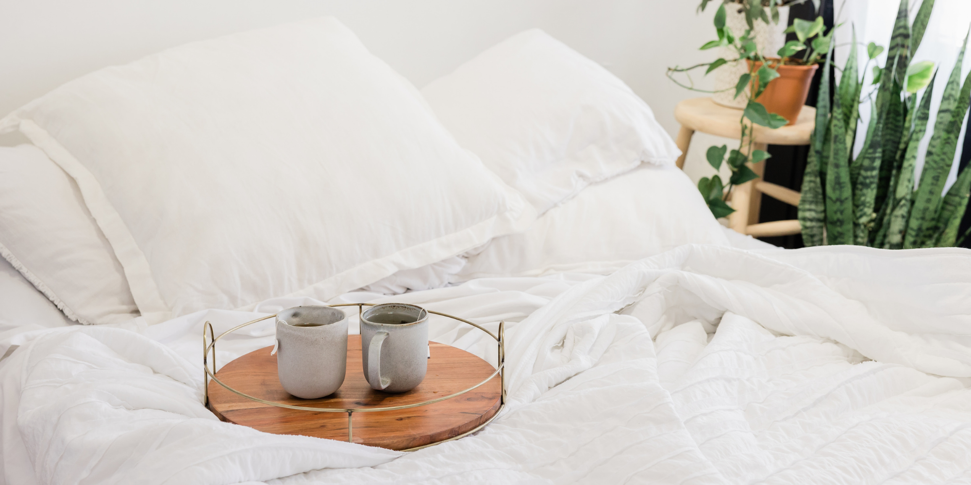 Morning tea ritual with two ceramic tea cups on a wooden tray placed on a soft white bed creating a calm and mindful daily tea moment