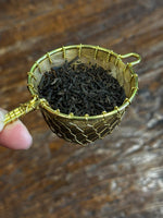 Organic Pu-erh loose leaf tea in a brass tea strainer, featuring aged fermented tea leaves known for their earthy, mellow flavor and smooth finish.