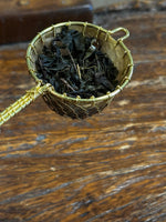 Organic fermented black tea leaves after steeping in a handcrafted brass tea strainer, showcasing fully expanded leaves with rich aroma and smooth character.