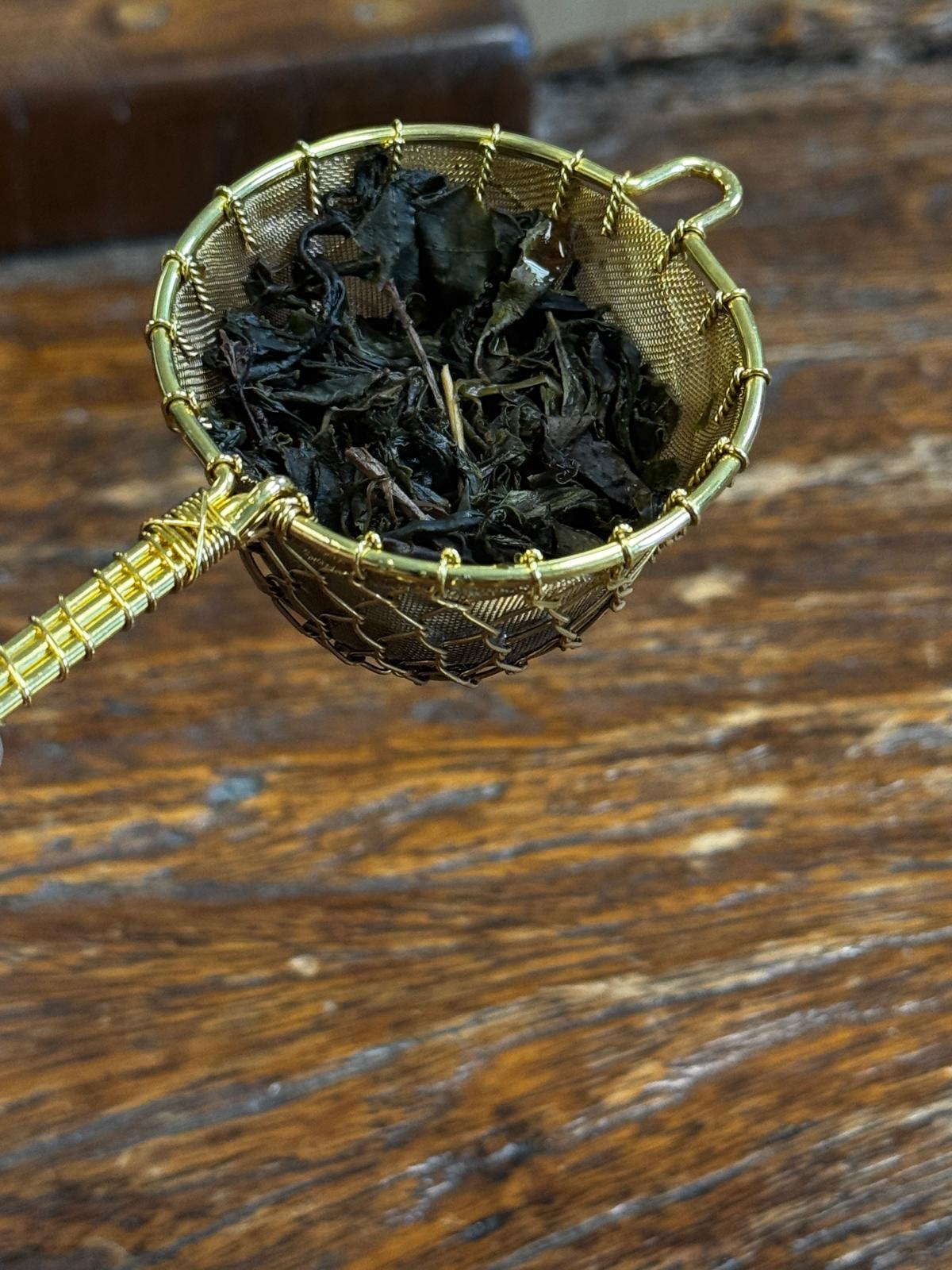 Organic fermented black tea leaves after steeping in a handcrafted brass tea strainer, showcasing fully expanded leaves with rich aroma and smooth character.