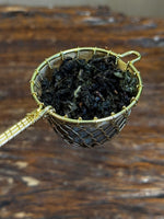 Organic Osmanthus Oolong loose leaf tea displayed in a handcrafted brass tea strainer, featuring dark rolled leaves with floral aroma and premium Taiwanese oolong character.