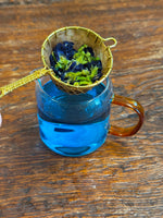 Whole butterfly pea flowers above a cup of vibrant blue butterfly pea tea, organic herbal infusion with natural color-changing properties.